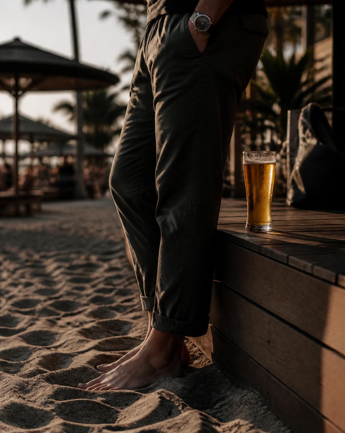 Pies en la arena junto a la terraza de madera con una cerveza